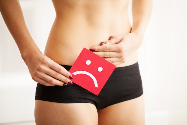 Conceito de infecção e problemas vaginais ou urinários. jovem mulher detém papel com sorriso triste acima da virilha Foto Premium