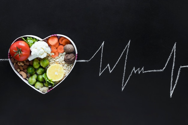 Conceito de vida saudável com legumes dispostos em heartshape como uma linha de vida ecg em fundo preto Foto gratuita