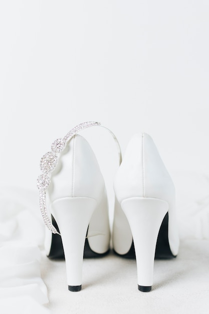 Coroa de diamante sobre o par de saltos altos de casamento branco contra o pano de fundo branco Foto gratuita
