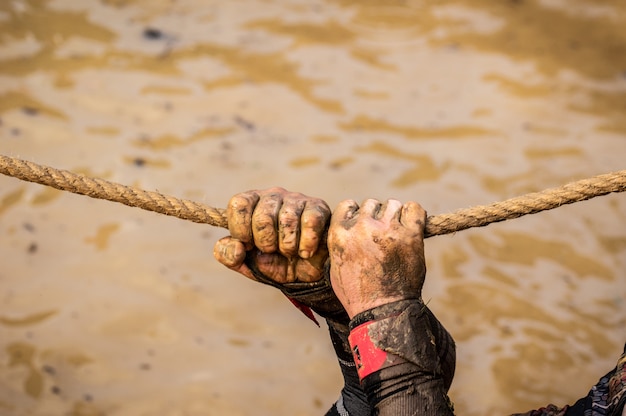 Corredores de corrida de lama, derrotando obstáculos usando cordas. detalhes das mãos. Foto Premium
