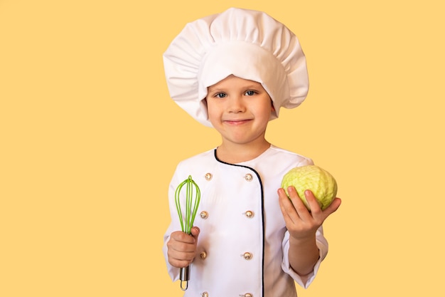 Criança sorridente uniforme branco do chef segurando um repolho e