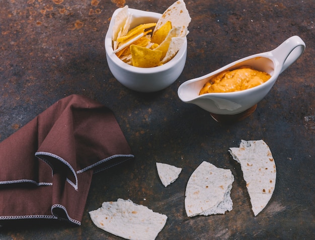 Deliciosa tortilla mexicana com nachos em tigela com molho de queijo e guardanapo sobre fundo enferrujado Foto gratuita