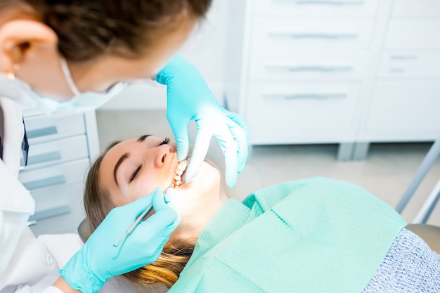 Dentista fêmea que verifica os dentes pacientes com cintas no escritório da clínica dental. Foto Premium