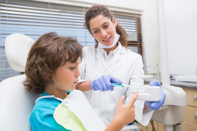 Dentista pediátrica mostrando garotinho como escovar os dentes na clínica odontológica Foto Premium