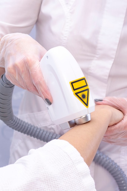 Depilação a laser e cosmetologia. a menina remove o cabelo no braço com um laser. procedimento de depilação em cosmetologia. depilação a laser e cosmetologia. conceito de cosmetologia e spa. foto vertical Foto Premium