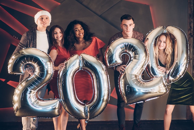 Desejando bem. grupo de jovens amigos lindos com números infláveis nas mãos comemorando o novo ano de 2020 Foto Premium