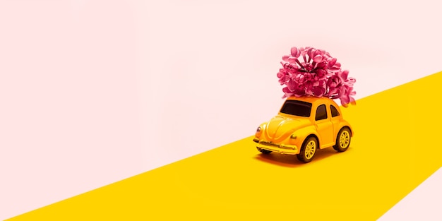Dia internacional da mulher feliz. brinque o carro amarelo com ramo de flor lilás em um fundo rosa com lugar para texto. Foto Premium