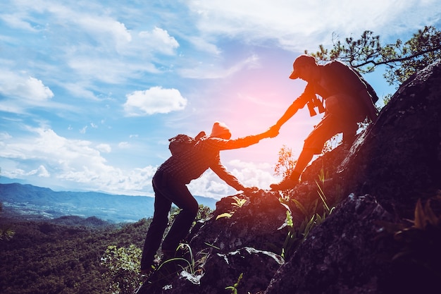 Dois amigos ajudando uns aos outros e com o trabalho em equipe tentando alcançar o topo das montanhas. Foto Premium