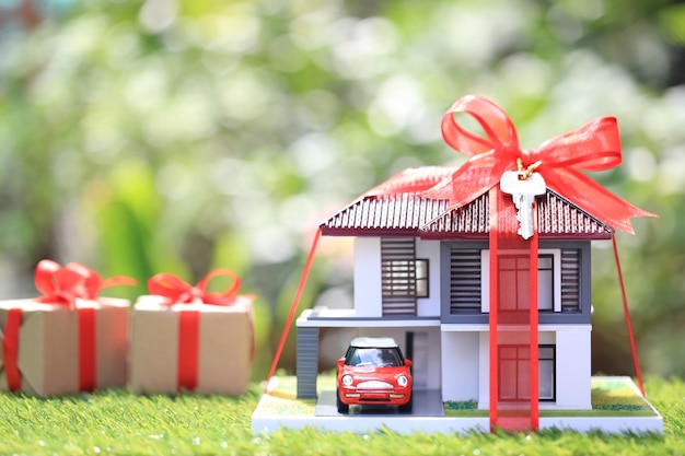 Dom nova casa e imóveis, casa modelo com fita vermelha e o carro em verde natural Foto Premium