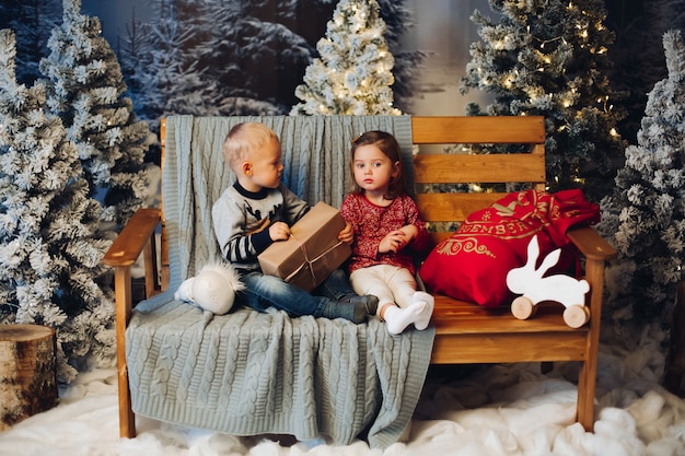 Duas crianças brincando com o natal perto de decoração e árvore de natal Foto Premium