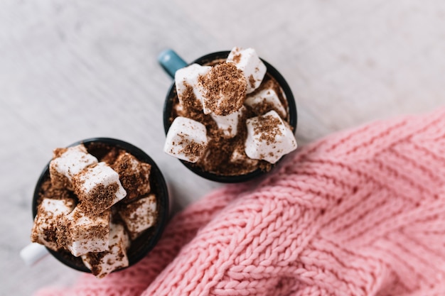 Duas xícaras com marshmallows e cachecol de malha Foto gratuita