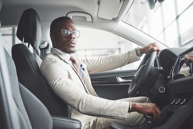 Elegante empresário negro sentado ao volante de um novo carro de luxo.  homem rico afro-americano. | Foto Grátis