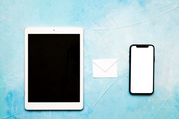Envelope de papel branco de ícones de mensagem com tablet digital e celular no pano de fundo azul pintado Foto gratuita