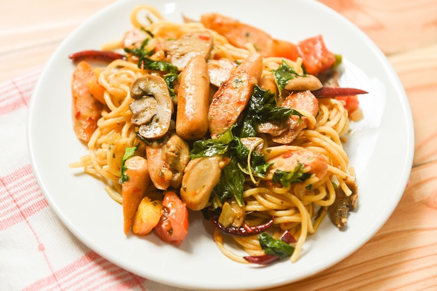 Espaguete quente e picante macarrão tomate pimentão e manjericão folhas vista superior - tradicional comida italiana deliciosa espaguete linguiça no prato sobre a mesa de jantar Foto Premium
