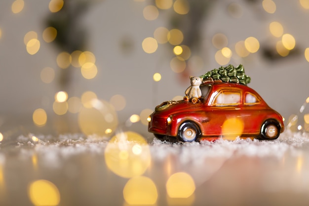 Estatuetas decorativas de um tema de natal. uma estatueta de um carro vermelho no qual um ursinho de pelúcia se senta. decoração da árvore de natal. decoração festiva, luzes quentes de bokeh. Foto Premium