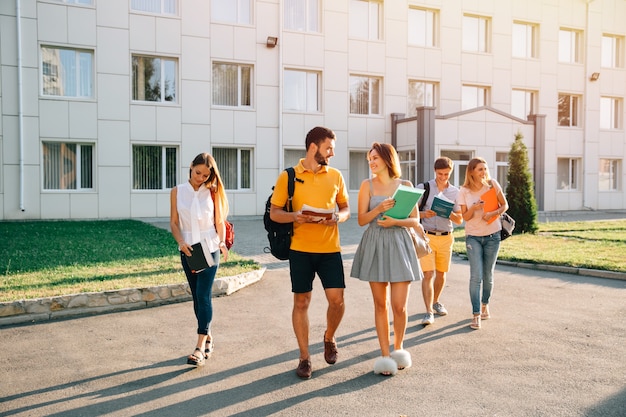 Estudantes universitários feliz com livros nas mãos caminhando juntos no campus Foto gratuita