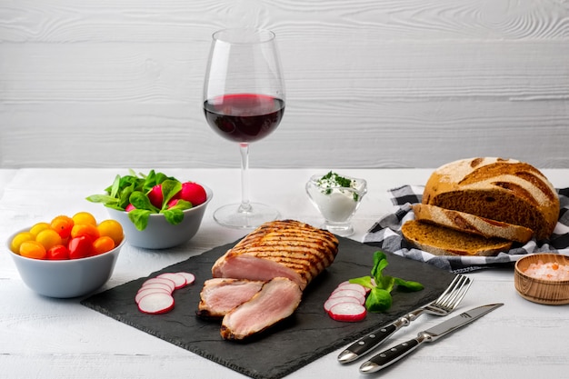 Faixa grelhada da carne de porco com os tomates frescos e o raddish servidos com vidro do vinho tinto. Foto Premium