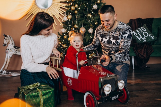 Família com filha pequena com presente de natal pela árvore de natal Foto gratuita