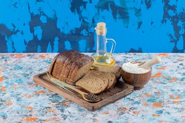Fatias de pão integral com farinha e garrafa de óleo na placa de madeira. Foto gratuita