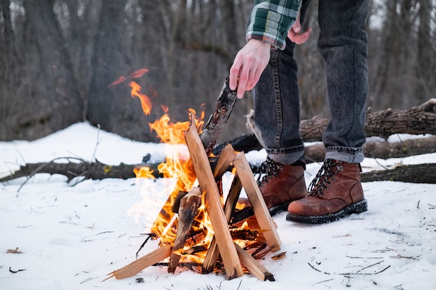 Fazendo uma fogueira em uma floresta de neve. indivíduo do sexo masculino perto de um incêndio em um dia de inverno na floresta | Foto Premium