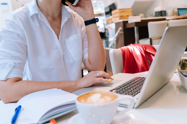 Feche acima da mulher de negócio das mãos que senta-se no escritório coworking e que datilografa em seu computador do teclado do portátil. Foto Premium