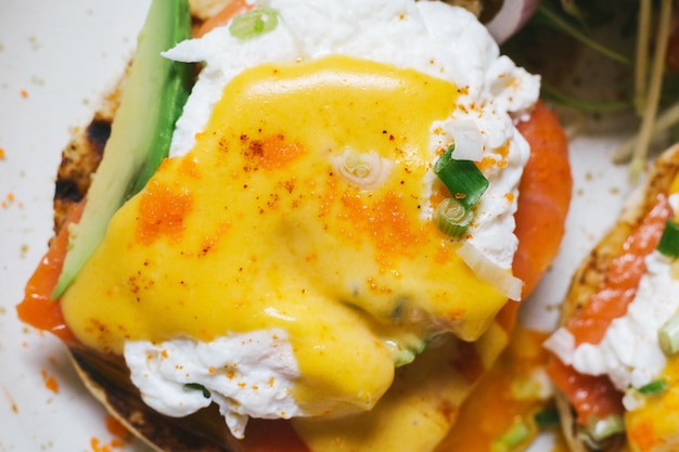 Feche acima da vista superior dos ovos benedict com salmões e abacate, servidos com salada na placa branca. Foto Premium