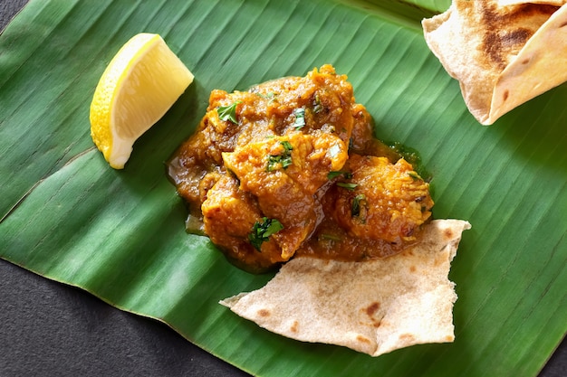 Feche acima do caril e do limão indianos tradicionais da galinha da manteiga servidos com pão do chapati na folha da banana. Foto Premium