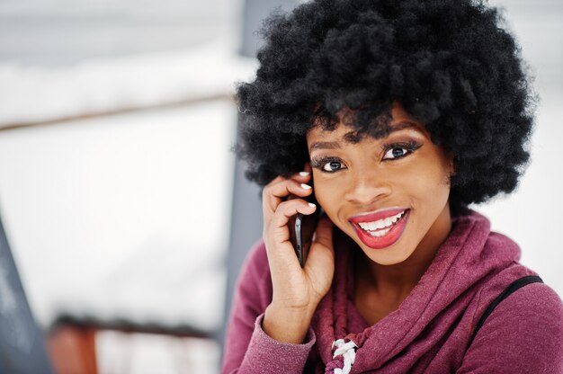Feche o retrato da mulher afro-americana de cabelos cacheados, posando em dia de inverno, falando no celular. Foto Premium
