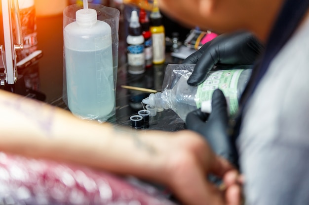 Feche o tatuador demonstra o processo de obtenção de tatuagem preta com tinta. mestre trabalha em luvas pretas estéreis. Foto Premium