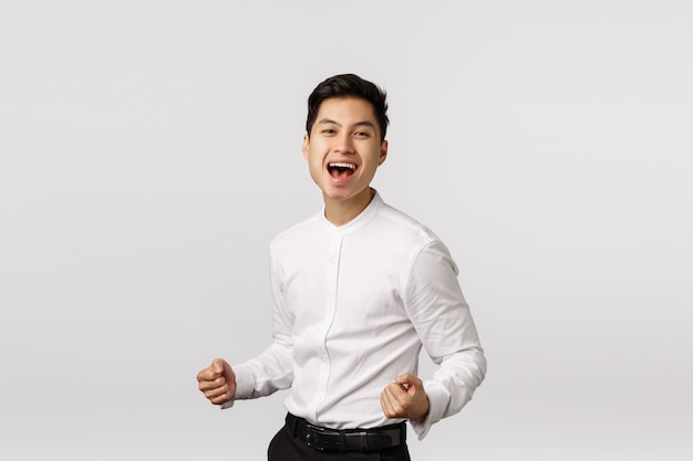 Feliz e bem-sucedido jovem empresário asiático cerra os punhos, acelera e sorri satisfeito, diga sim, comemorando a vitória, fez uma boa oferta, alcance a meta, regozija-se com o prêmio, Foto Premium