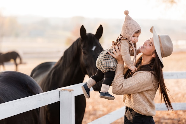 Feliz Jovem Mae Esta Brincando Com A Filha Bebe Perto Dos Cavalos No Parque Outono Foto Premium