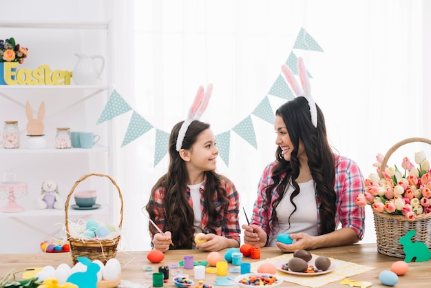 Feliz mãe e filha pintando os ovos de páscoa com escova em casa Foto gratuita
