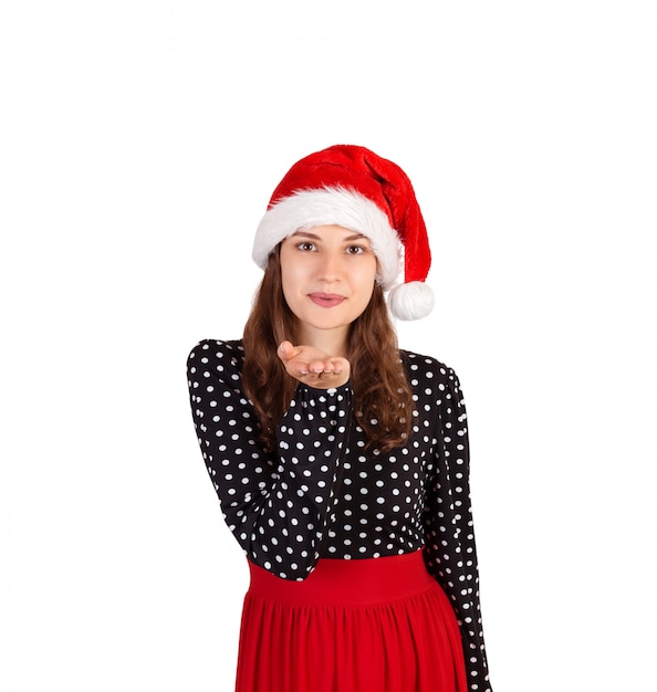 Feliz mulher de vestido sopra um beijo do ar para a câmera. garota emocional no chapéu de natal papai noel isolado Foto Premium