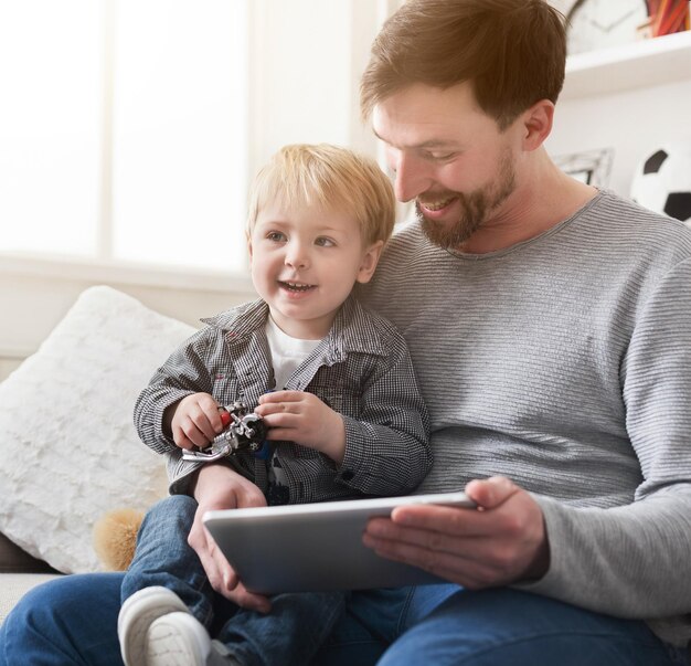 Feliz Pai E Filho Brincando Em Um Tablet Digital Sentados No Sofá Em Casa Foto Premium 