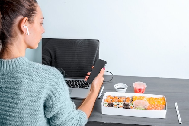 Feminino mão segurando o telefone com tela de comida de entrega app e laptop local de trabalho sem fio do escritório Foto Premium