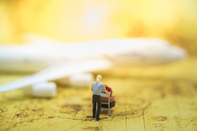 Figura diminuta masculina com carro e bagagem do aeroporto no mapa do mundo com modelo do avião. Foto Premium