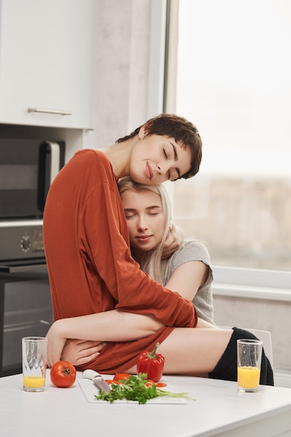 Foto Horizontal De Duas Mulheres Abraçando Na Cozinha Com Os Olhos Fechados E Um Sorriso Sensual 8748