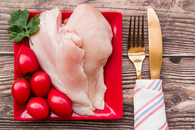 Frango cru e tomates no prato com garfo e faca Foto gratuita