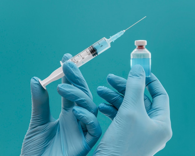 Frasco de vacina e seringa segurados por médico com luvas Foto gratuita