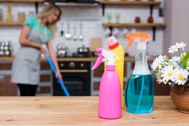 Frascos de detergente e spray na mesa de madeira na frente da mulher deprimida em casa Foto gratuita