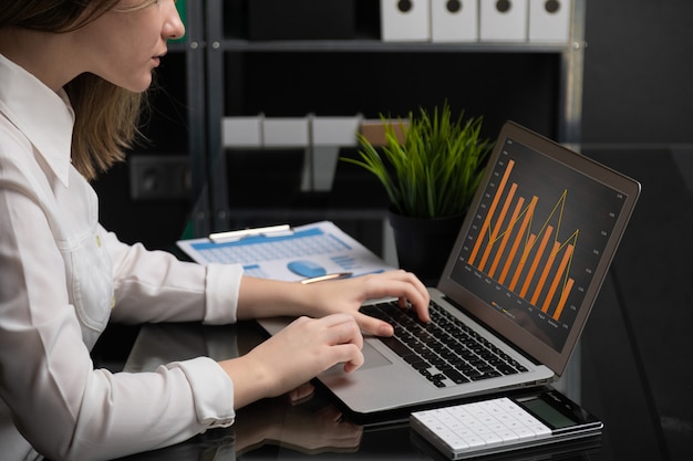 Freelancer digitando no laptop com tela preta em branco próximos gráficos e calculadora Foto Premium