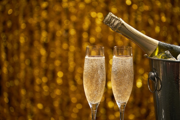 Garrafa de champanhe em um balde com gelo e duas taças de champanhe no fundo dourado bokeh Foto Premium
