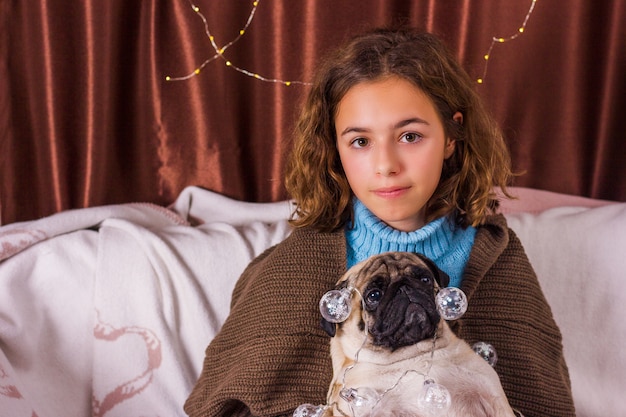 Guirlanda de chistmas no cão pug. menina encantadora com um pug muito engraçado. menina encaracolada abraça um pug Foto Premium