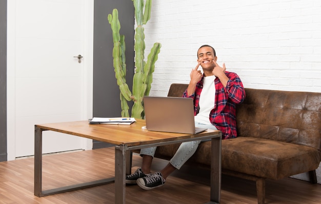 Homem americano africano, com, laptop, em, a, sala de estar, sorrindo, com, um, feliz, e, agradável, expressão Foto Premium
