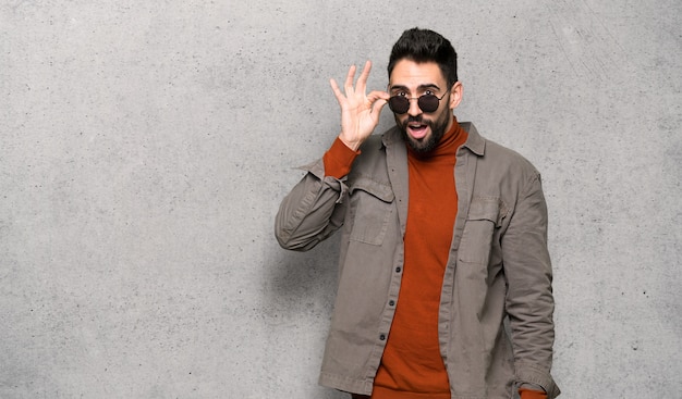 Homem bonito com barba com óculos e surpreso ao longo da parede texturizada Foto Premium