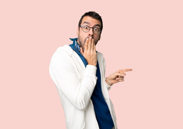 Homem bonito com óculos, apontando o dedo para o lado com uma cara de surpresa no fundo rosa isolado Foto Premium