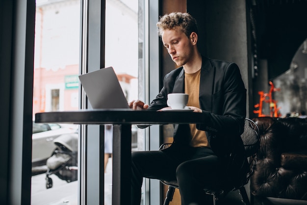 Homem bonito, trabalhando em um computador em um café e beber café Foto gratuita