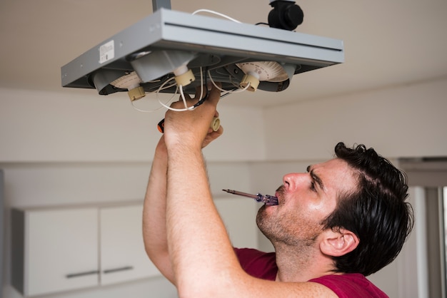 Homem, carregar, tester, em, boca, enquanto, reparar, teto, foco, luz, casa Foto gratuita