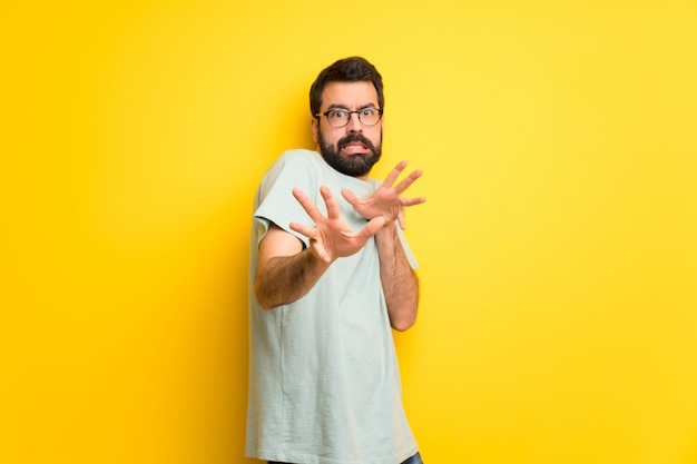 Homem com barba e camisa verde é um pouco nervoso e assustado esticando as mãos para a frente Foto Premium