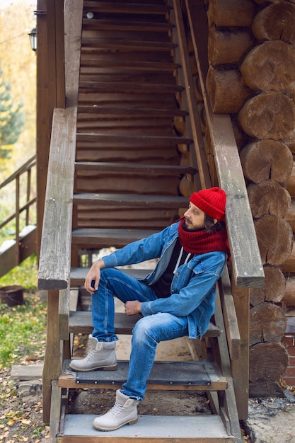 Homem Com Uma Barba Hipster Em Um Chapéu De Malha Vermelho E Uma Jaqueta Jeans Está Sentado Na 